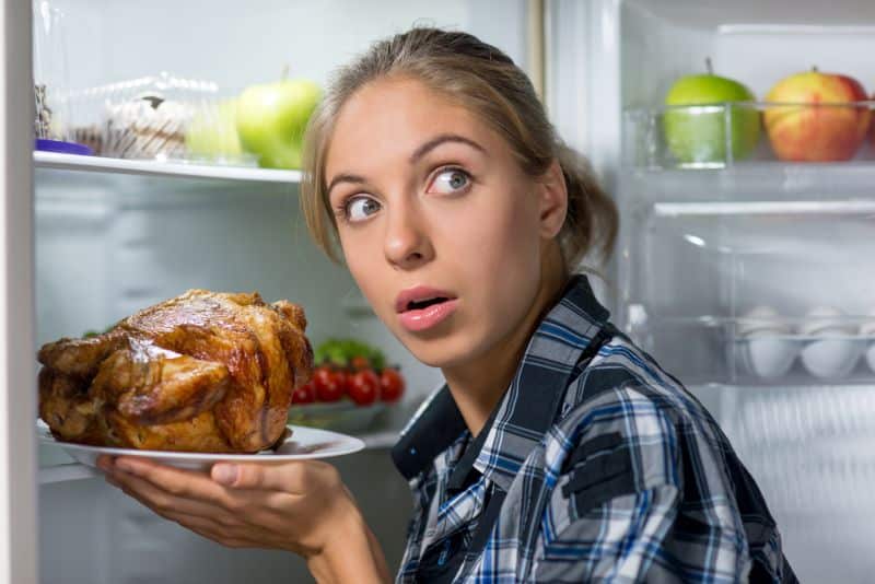 Woman holding fried chicken near opened refrigerator